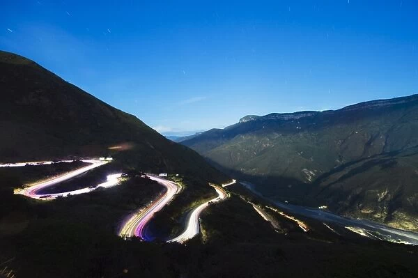 Moonlit valley and car light trails on a winding road in Chicamocha National Park