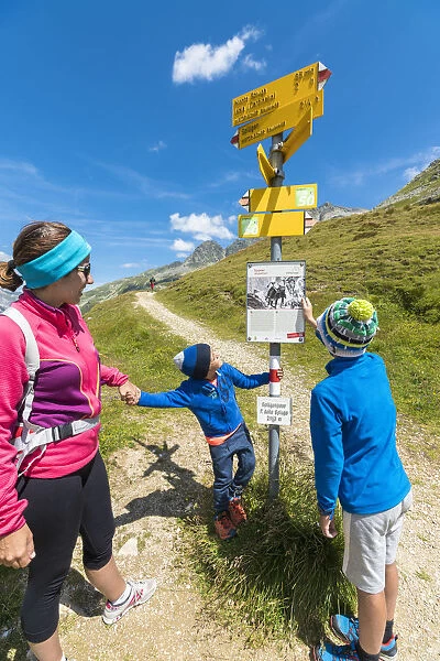 Mother and sons look at the signpost of hiking trails, Spluga Pass, Chiavenna Valley