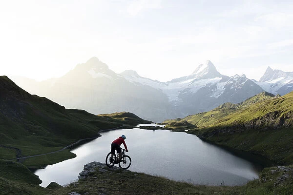 Mountain biker riding downhill at Bachalpsee lake at dawn, Grindelwald, Bernese Oberland