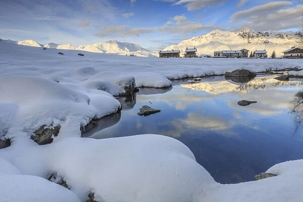 Mountain huts and reflections in Lago Azzurro surrounded by snow, Spluga Valley