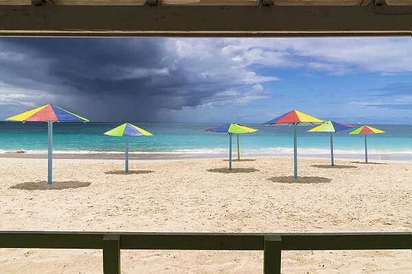 Multicolored striped umbrellas on white sand beach under storm clouds, Antigua, West Indies, Caribbean, Central America