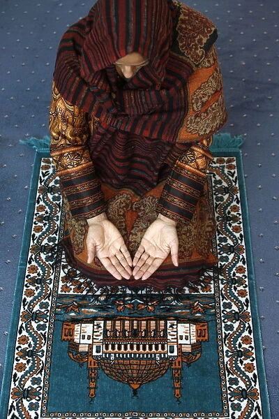 Muslim woman kneeling on prayer mat saying prayers, Jordan, Middle East