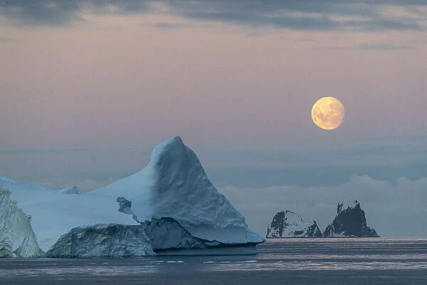 Nearly full moon setting over small islands and icebergs off the Trinity Peninsula