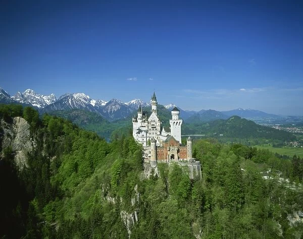 The Neuschwanstein Castle on a wooded hill with mountains in the background