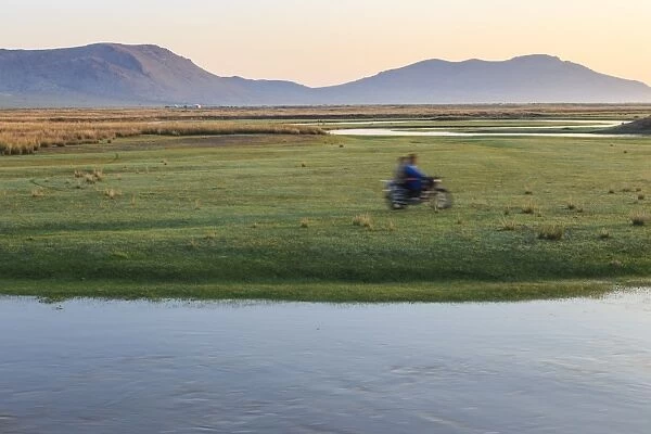 Nomads on motorcycle pass in a blur, river and distant gers, dawn, Nomad camp, Gurvanbulag