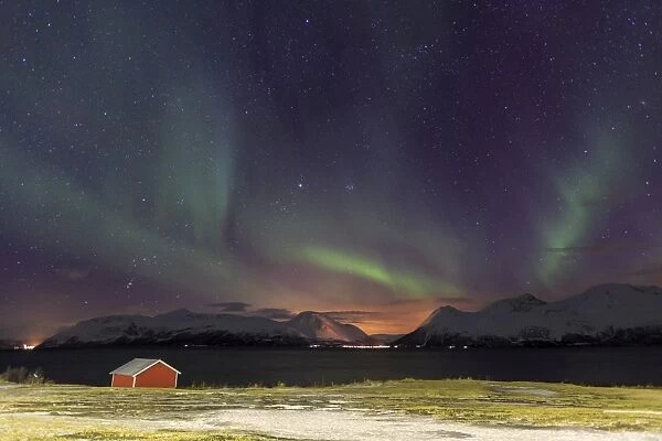 Northern Lights illuminates the wooden cabin at Svensby, Lyngen Alps, Troms, Lapland