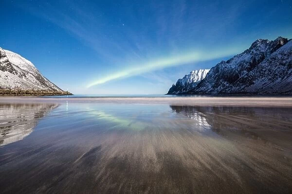 Northern lights and stars light up the sandy beach framed by snowy peaks, Ersfjord