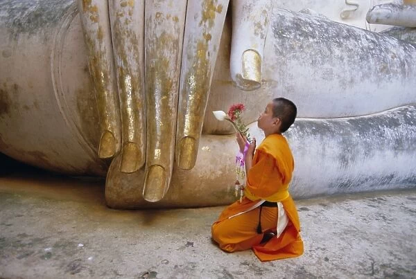 Novice Buddhist monk kneeling beneath the Phra Atchana Buddha statue