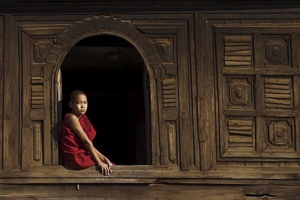 Novice monk sitting in window of 18th century wooden monastery of Nat Taung Kyaung
