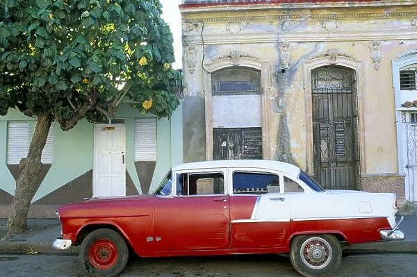 Old American car parked on street beneath fruit tree, Cienfuegos, Cuba