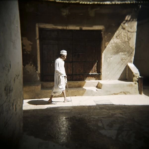 Old man walking down shady street in traditional white robes, Stone Town
