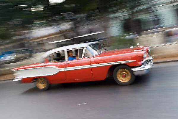 Old vintage American red and white car driving along a street in Havana, Cuba, West