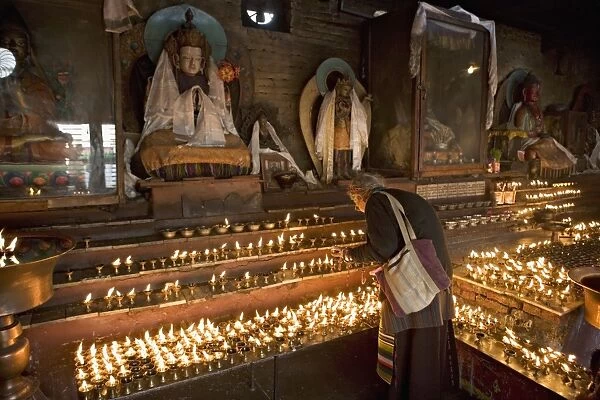 Old woman lighting butter lamps in front of Buddha