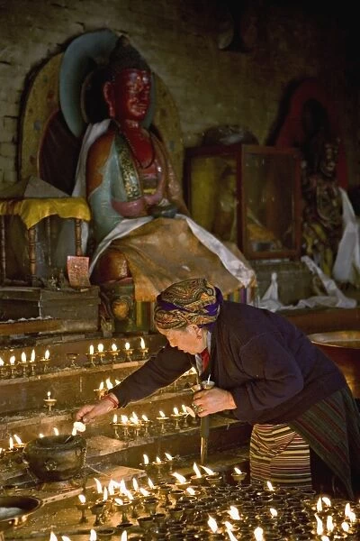 Old woman lighting butter lamps in a small temple on
