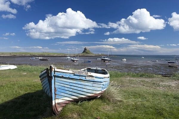 Old wooden fishing boat on a grassy bank with Lindisfarne harbour and Lindisfarne Castle in the background, Holy Island (Lindisfarne), Northumberland, England, United