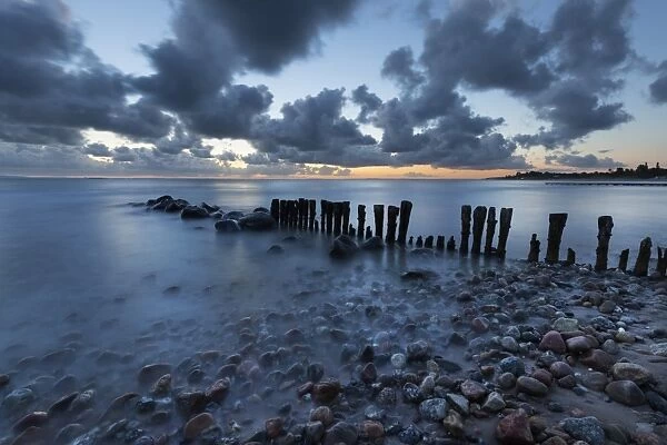 Old wooden piles going out to sea and pebbles on beach at dawn, Munkerup, Kattegat Coast
