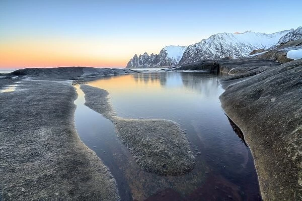 Orange sky at sunset reflected on snowy peaks and the frozen sea surrounded by rocks Tungeneset