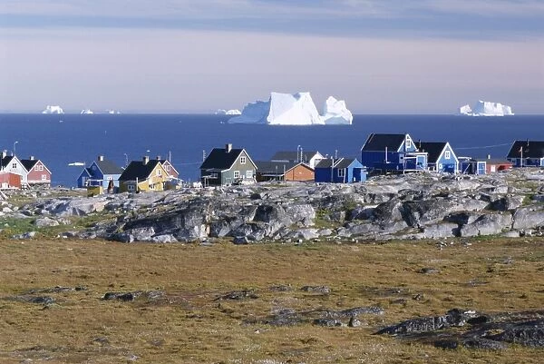 Painted village houses in front of icebergs in Disko Bay