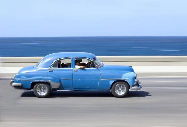 Panned shot of old blue American car to capture sense of movement, with the Caribbean Sea in the background, The Malecon, Havana Centro, Cuba, West Indies, Central America
