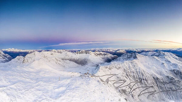 Pano by drone of sunrise over the narrow bends of Stelvio Pass mountain road covered