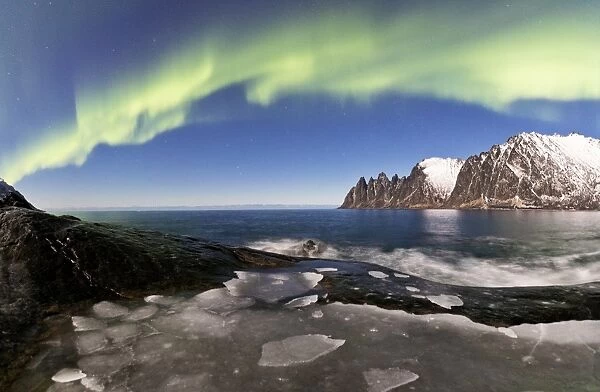 Panorama of frozen sea and rocky peaks illuminated by the Northern Lights (aurora borealis)