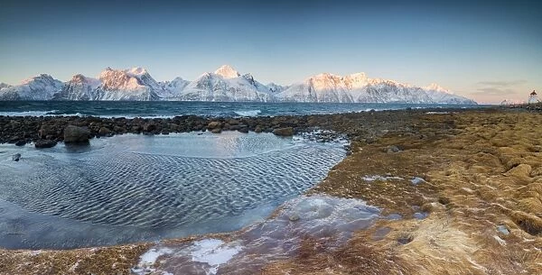 Panorama of frozen sea and snowy peaks at dawn surrounded by rocks covered with ice
