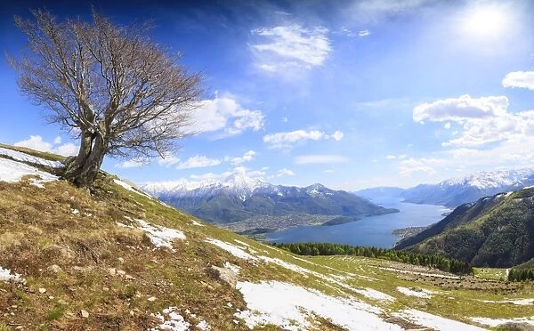 Panorama of meadows partially covered with snow with Lake Como on the background