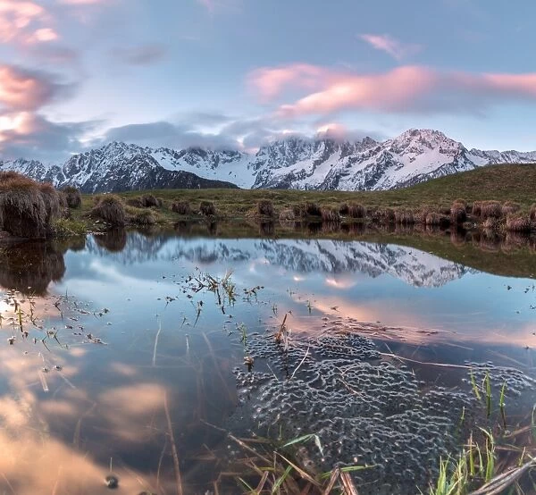 Panorama of pink clouds reflected in water at dawn, Tombal, Soglio, Bregaglia Valley