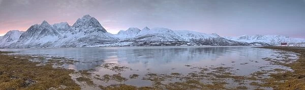Panorama of pink sky at dawn on snowy fields and wooden hut surrounded by frozen sea