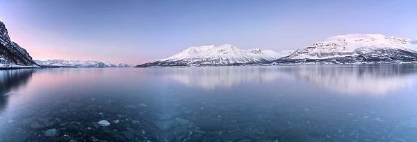 Panorama of pink sky and snowy peaks reflected in the frozen sea at sunset, Manndalen