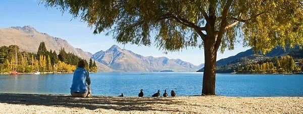 Panorama of a tourist relaxing by Lake Wakatipu in autumn at Queenstown, Otago, South Island, New Zealand, Pacific