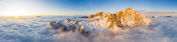 Panoramic aerial view of Grigne group mountain peaks emerging from mist at sunset