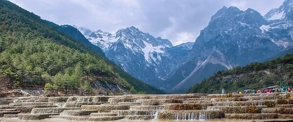 A panoramic view of cascading waterfalls and mountain backdrop, including Yu Long Xue Shan at White Water River (Baishuihe), Lijiang, Yunnan, China, Asia