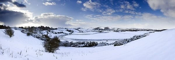 Panoramic view of snow-covered landscape beneath blue winter sky looking towards meandering River Aln, Lesbury, near Alnwick, Northumberland, England, United