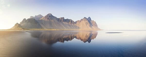 Panoramic view of Vestrahorn Mountain range reflecting in shallows of black volcanic beach