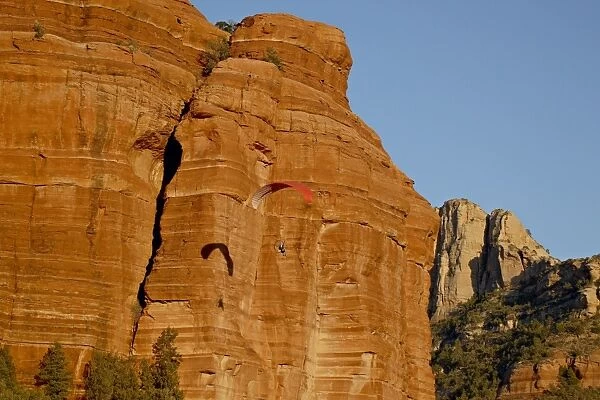 A paraglider flies past a red rock formation, Coconino National Forest