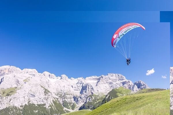 A paraglider among rocky peaks and green meadows Doss Del Sabion, Pinzolo, Brenta Dolomites