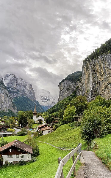 Path among green meadows of the alpine village of Lauterbrunnen with Trummelbach Falls in the background, Bern canton, Switzerland, Europe