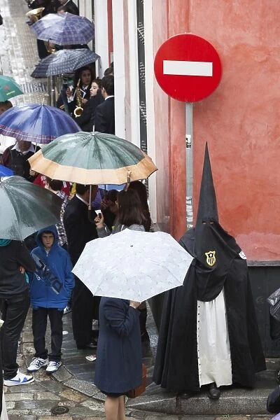Penitent during Semana Santa (Holy Week) along rainy street, Seville, Andalucia, Spain, Europe