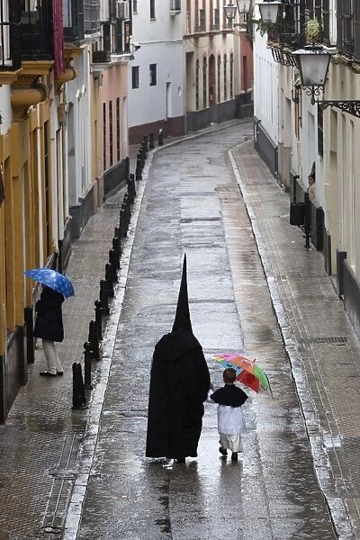 Penitents during Semana Santa (Holy Week) along rainy street, Seville, Andalucia, Spain, Europe