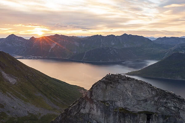 People admiring the sky at dawn standing on mountain top above the fjords, Senja island