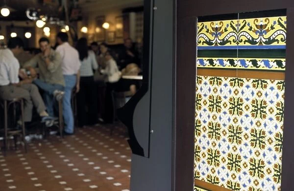 People inside a tapas bar and a detail of decorative tiled wall