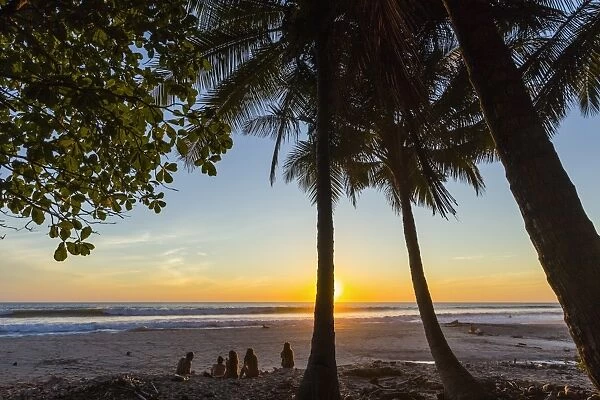 People by palm trees at sunset on Playa Hermosa beach, far south of the Nicoya Peninsula