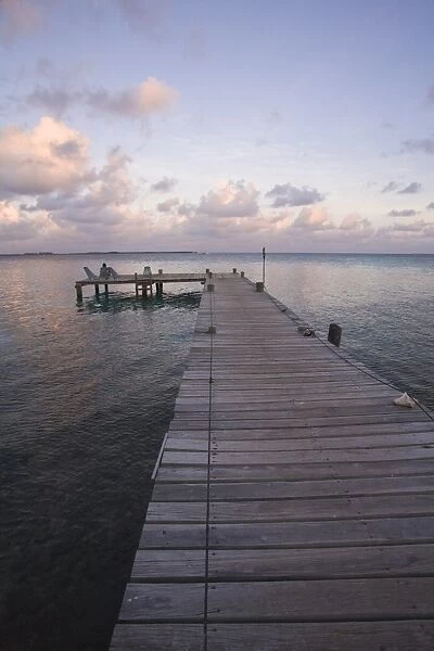 People sitting on chair on jetty at sunrise, Tobaco Caye, Belize, Central America