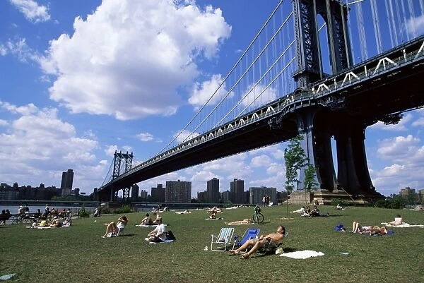 People sunbathing at a park in Brooklyn under the Manhattan Bridge