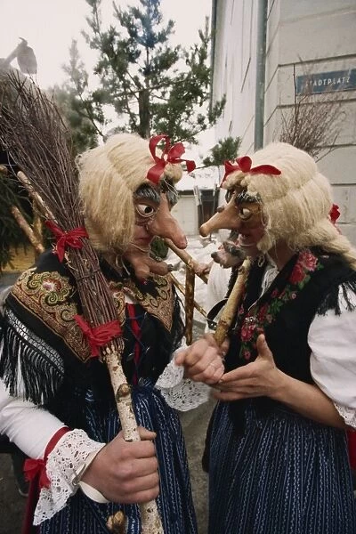 Two people wearing masks and traditional dress, one carrying a broomstick