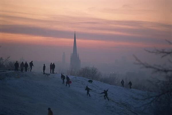 People in a winter landscape with snow on the ground and Norwich Cathedral in the background