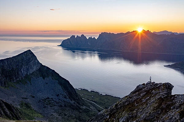 Person admiring the fjord at dawn standing on top of Husfjellet mountain, Senja island