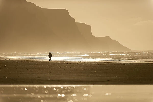 Person walking along beach in the evening sunlight, Rhossili, Gower Peninsula, Swansea