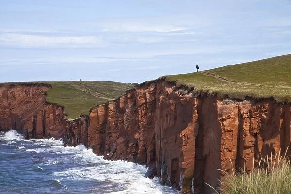Person walking on red sandstone cliff on Cap-aux-Meules Island in the Iles de la Madeleine